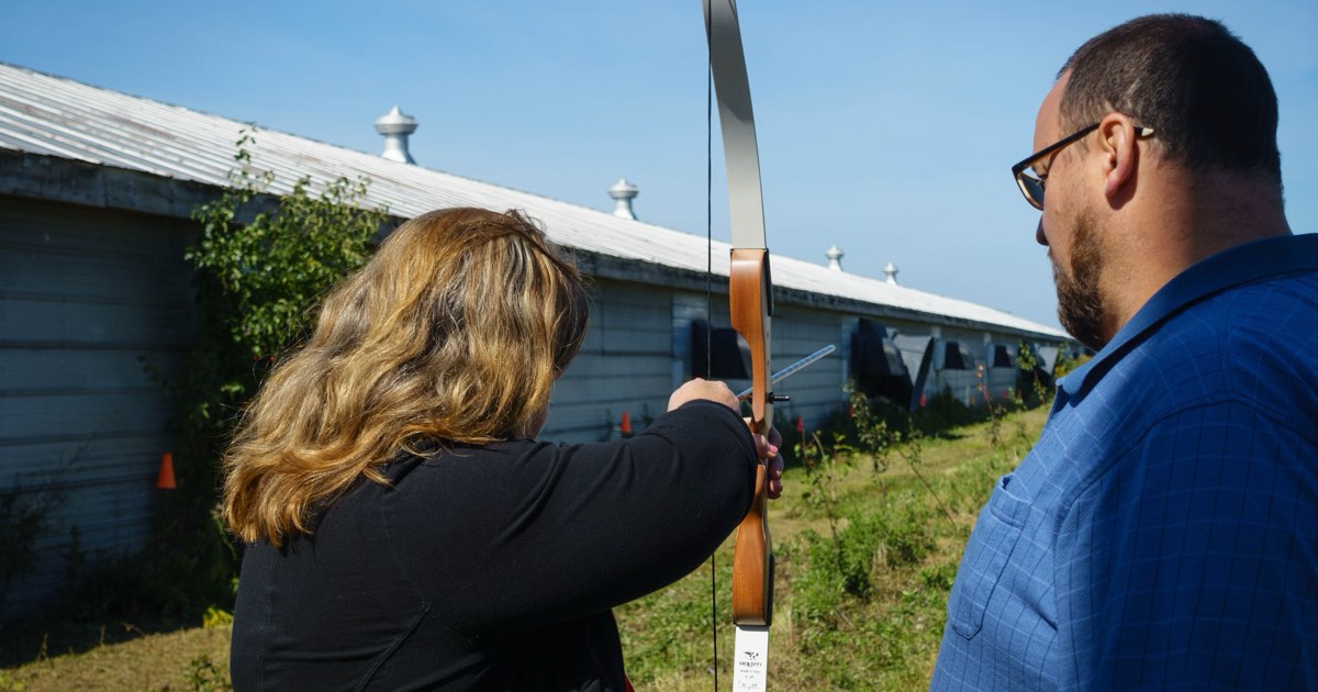 A coach watching an archer draw a recurve bow during a lesson