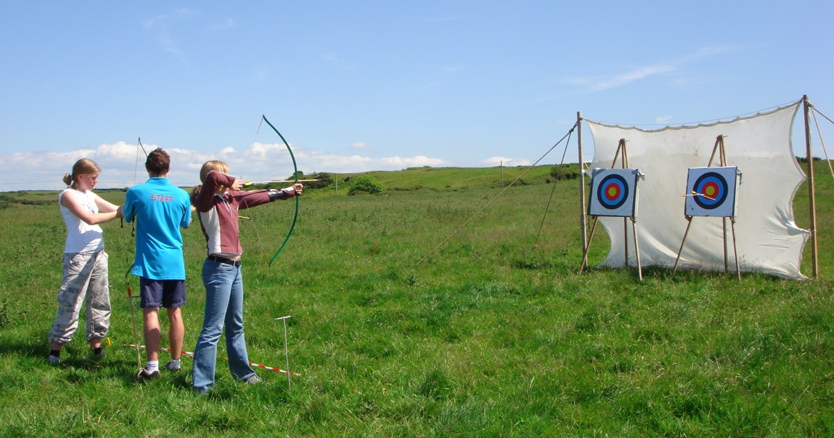 An archery lesson on an open field with targets set against a tall safety net