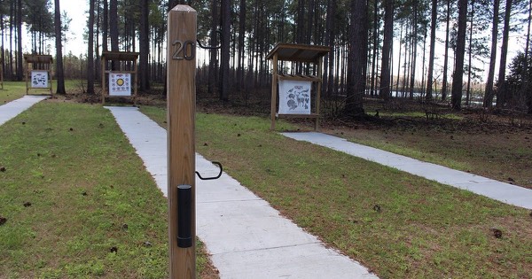 Outdoor archery range with covered target stands at marked distances under pine trees
