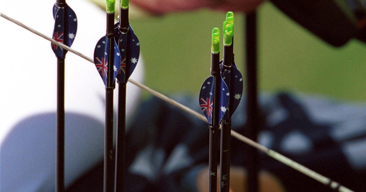 Archer holding carbon arrows with bright green fletching beside a recurve bow