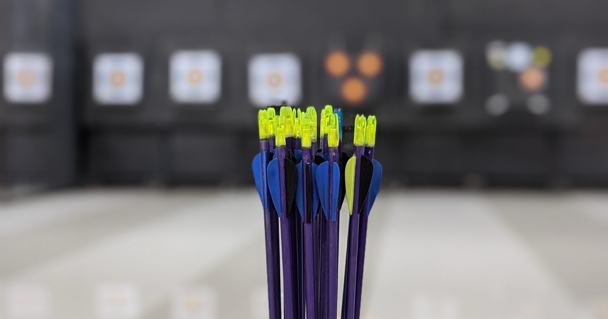 Bundle of arrows with bright fletchings in front of an indoor archery range