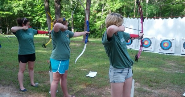 Archers practising at an outdoor range with targets and a backstop net behind them