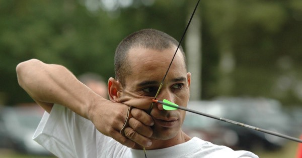 Barebow archer at full draw with the string near the corner of the mouth at a field archery championship