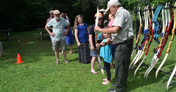 An instructor helping a young archer at a beginner archery session beside a rack of club recurve bows