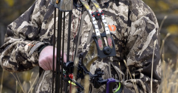 A bowhunter in camouflage holding a compound bow fitted with sight and quiver