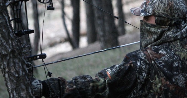 Close-up of a camouflaged bowhunter with a face mask at full draw with a compound bow