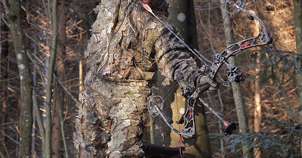Bowhunter in a leafy camouflage suit standing on a tree stand with a compound bow