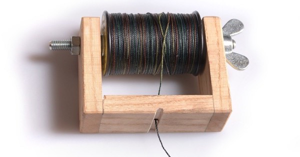 Wooden bowstring serving tool holding a spool of dark serving thread, with the thread running out through a slot in the base