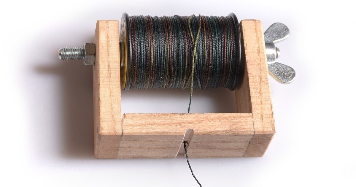 Wooden bowstring serving tool holding a spool of dark serving thread, with the thread running out through a slot in the base