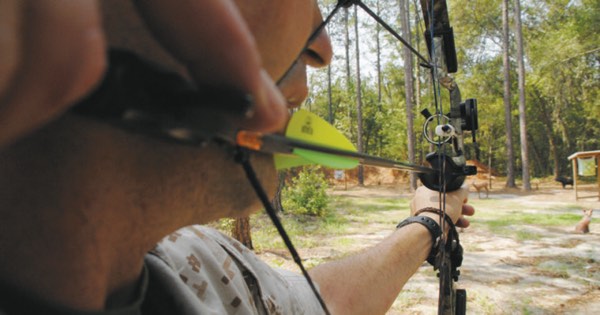 Close-up of an archer at full draw with a compound bow, the string touching the face at the anchor point