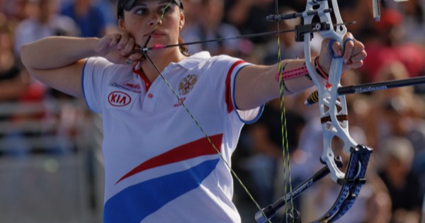 A compound archer at full draw with a release aid in front of a large crowd at a World Cup event