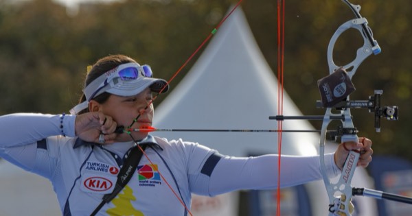 Compound archer at full draw with peep sight, scope and release aid at a competition