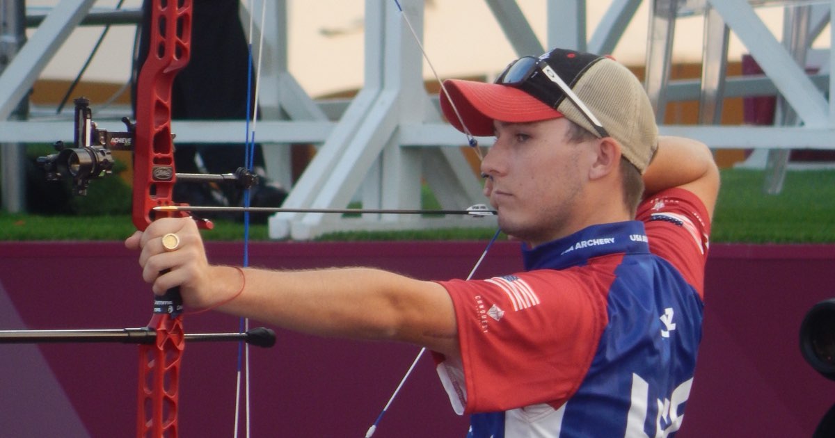 A compound archer at full draw with a red target bow and stabiliser