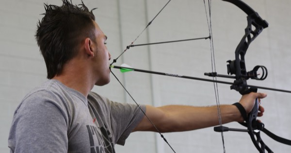 A compound archer at full draw with the sight housing and pin visible in front of the riser