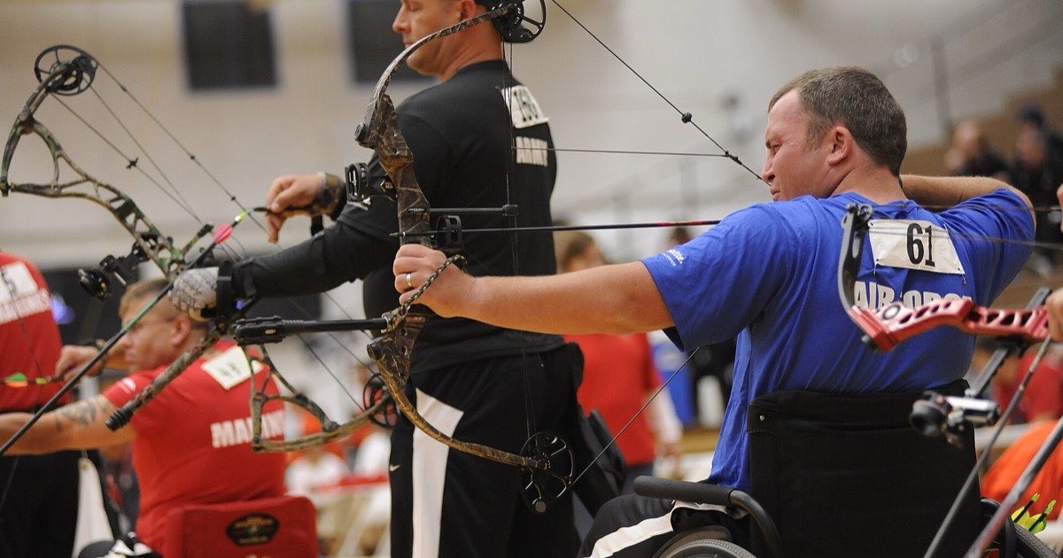 Compound archers at the shooting line during an indoor competition, one at full draw
