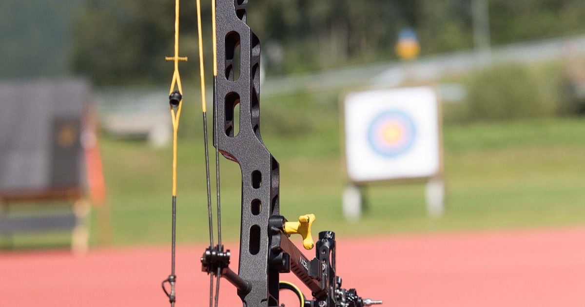 Compound bow string with a peep sight tied into the strands, the sight and riser beside it and a target in the background