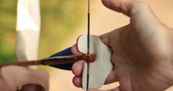 Close-up of an archer's drawing hand with a leather finger tab on the string at anchor