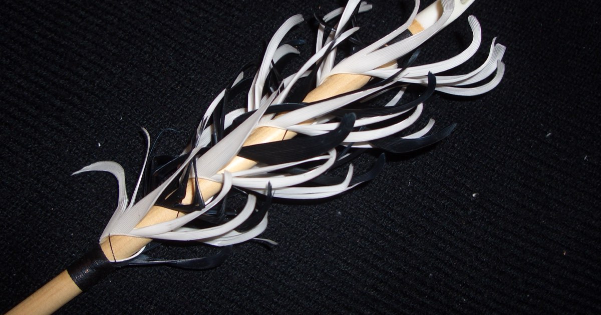 Close-up of a spiral flu-flu fletching made of white and black feathers on a wooden arrow