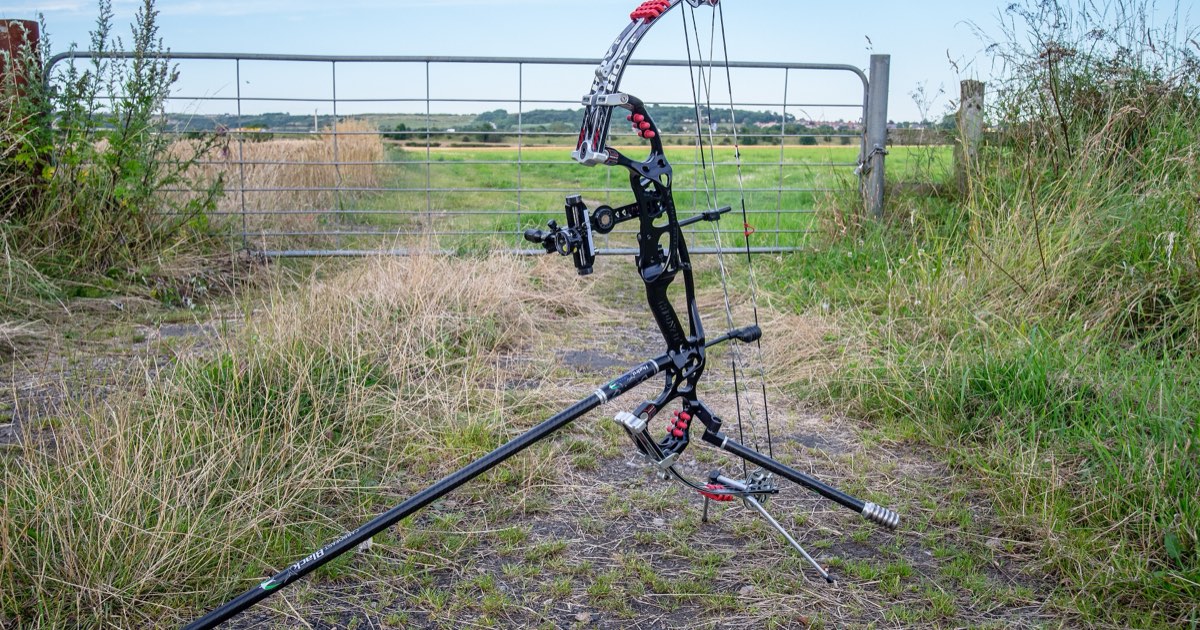 A Hoyt compound bow with sight and stabiliser standing on a farm track in front of a field gate