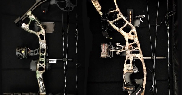 Two camouflage hunting compound bows laid in a bow case, each with a pin sight and arrow rest fitted to the riser