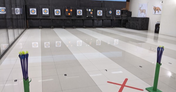 Indoor archery range with arrows in floor stands at the shooting line and target faces on the wall