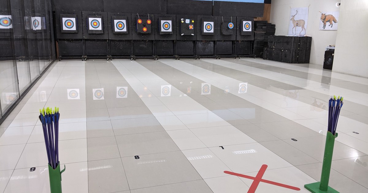 Indoor archery range with arrows in floor stands at the shooting line and target faces on the wall