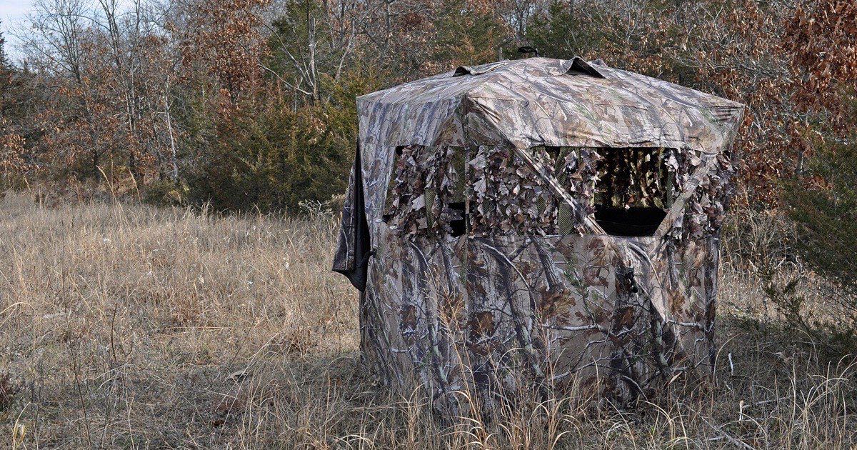 Camouflage pop-up hunting blind set up in tall grass at the edge of autumn woods
