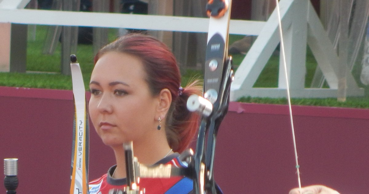Recurve archer at the shooting line with the riser, sight and clicker visible on an Olympic-style bow