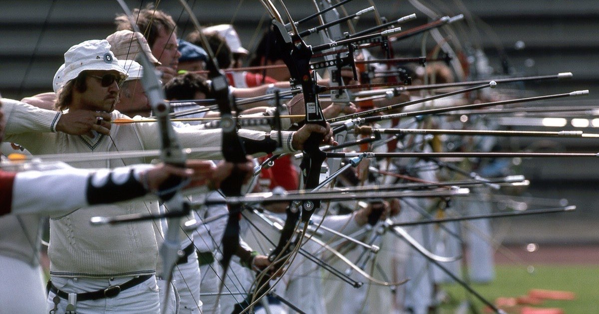 Line of recurve archers at full draw at a 1983 tournament in Germany, with long front stabilisers extending from their bows