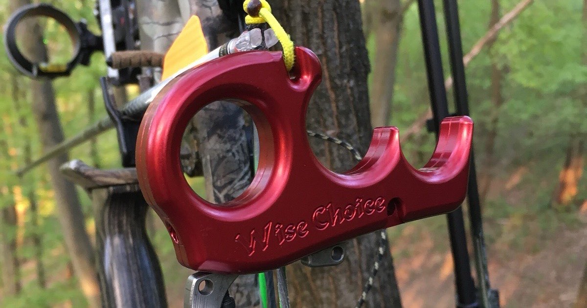 Hand-held release aid hanging from a compound bow next to a tree
