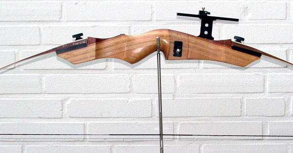 A Samick takedown recurve bow with a wooden riser and bolt-on sight hanging on a white brick wall
