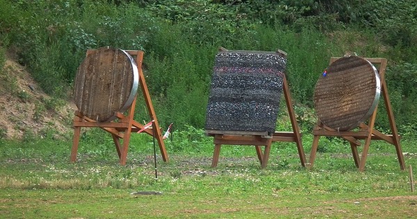 Two round straw target bosses and a layered foam target on wooden stands at an outdoor range